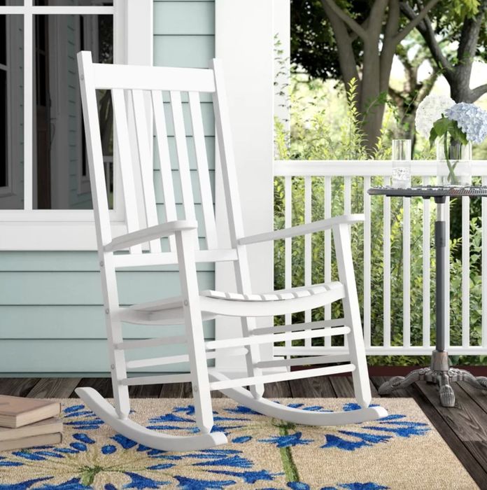 A white rocking chair placed in a beautifully decorated porch area, offering a cozy spot to relax and unwind.