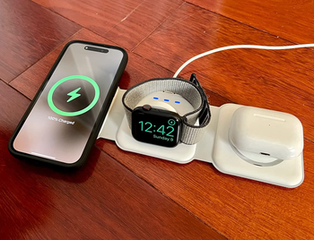 A white wireless charger laid out, charging a phone, watch, and AirPods simultaneously