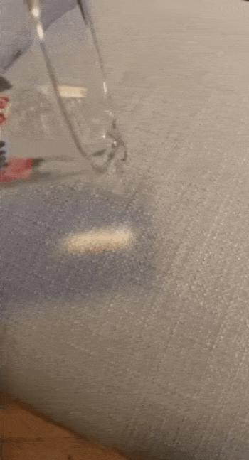 A reviewer demonstrating how water rolls off their couch after using the repellent spray, showcasing the fabric's resistance to spills