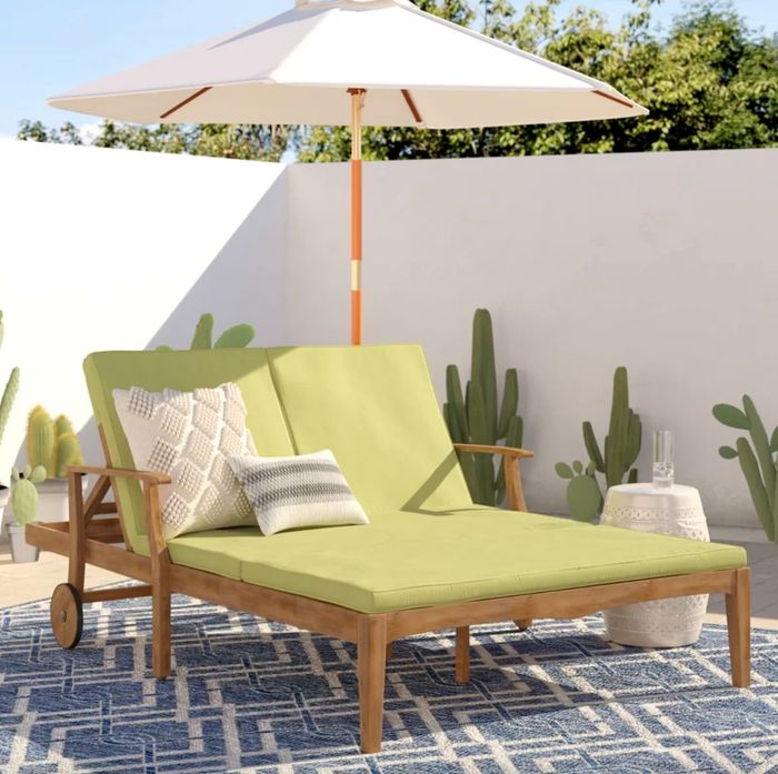 a light wood double chaise lounge with a green frame and decorative pillows, placed in an inviting outdoor setting