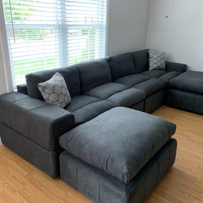 A modern L-shaped sectional sofa with two patterned cushions, positioned near a window in a stylish living room.