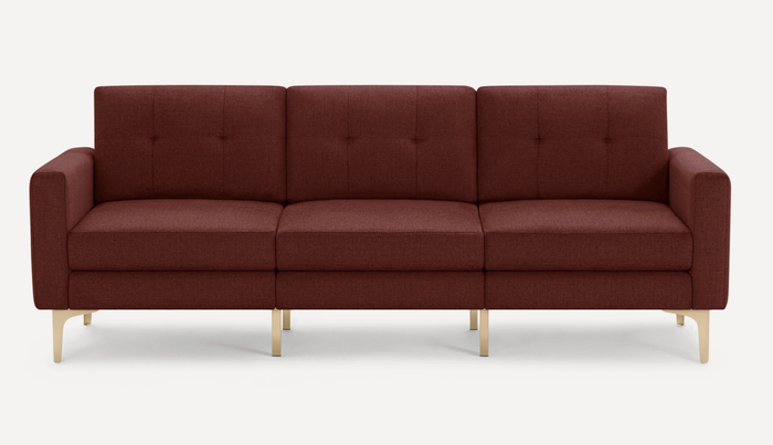 A dark red sofa with elegant gold legs sits in a stylish space