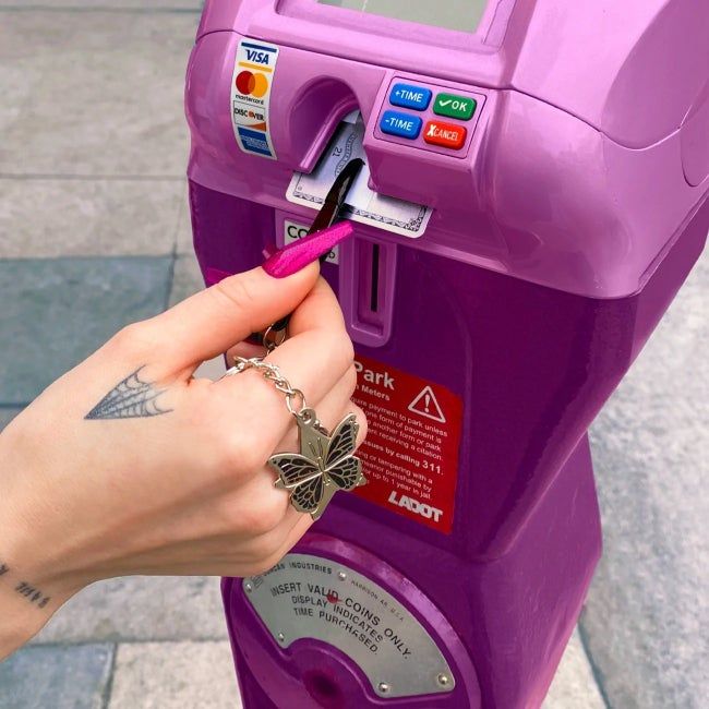 A person using the tweezer keychain to retrieve their credit card from a parking meter.