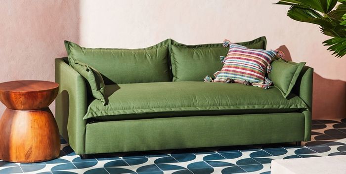 A green sofa with a striped cushion placed beside a wooden stool on a patterned floor