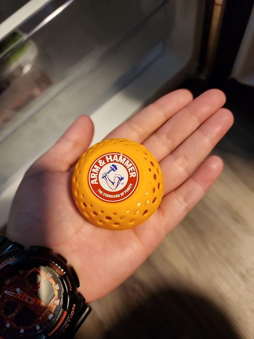 A close-up shot of a hand gripping an Arm & Hammer laundry scent booster ball.
