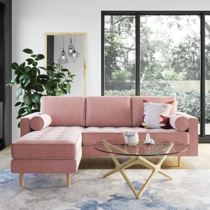 A pink velvet sectional with natural wood legs, shown in a chic living room setup