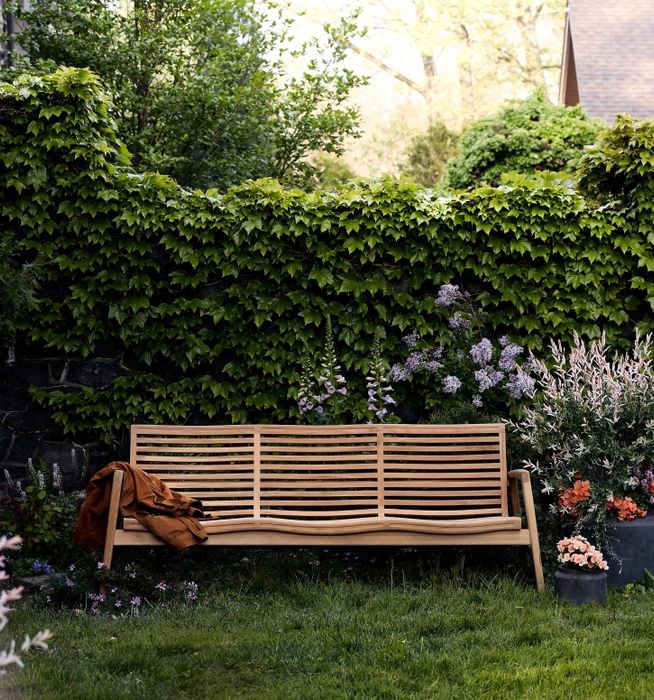 A wooden garden bench with a brown jacket draped over it, nestled in a lush garden with green ivy and colorful flowers.