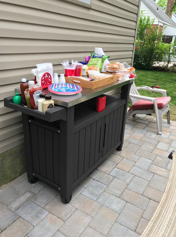 A cart filled with paper plates, napkins, cups, condiments, and various food and party essentials.