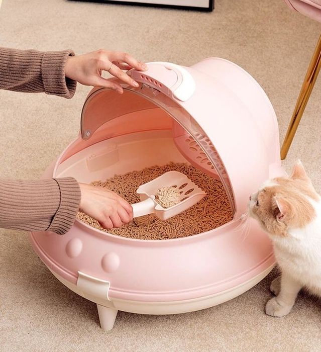 Someone is scooping litter from a pink UFO-shaped cat box.