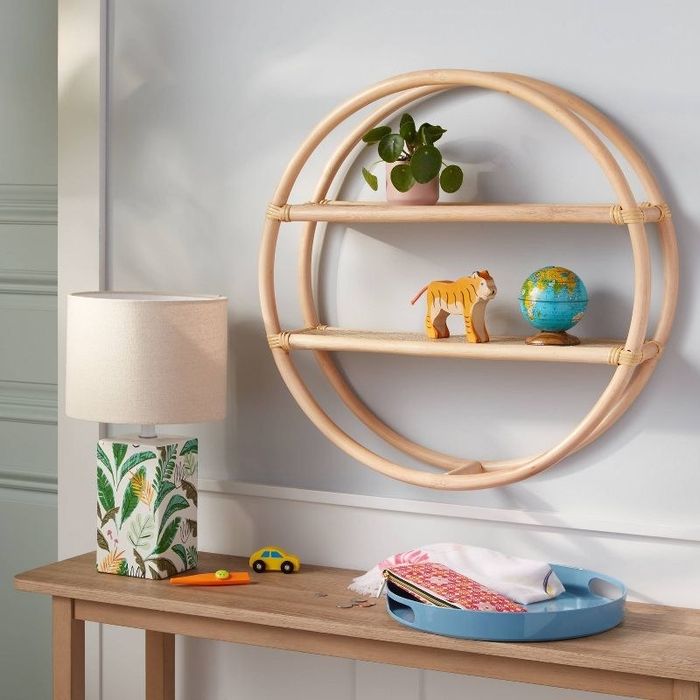 A round rattan wall shelf with two tiers, showcasing trinkets on top of a narrow table.