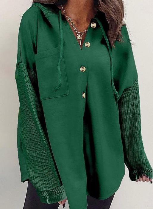 A person wearing a stylish long-sleeve button-up shirt made of a mix of knit and fabric textures, accessorized with a chain necklace.
