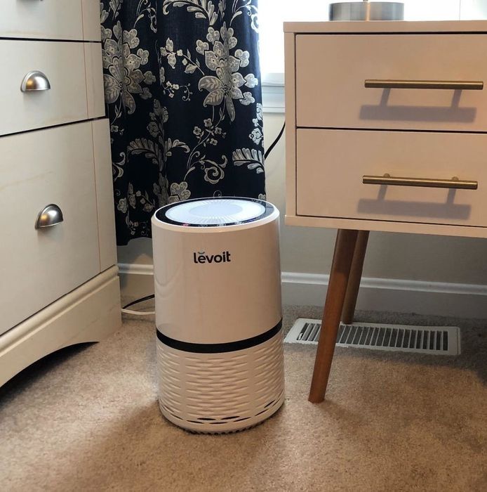 A white air purifier placed beside a nightstand, blending seamlessly into the room.