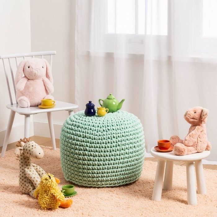 A mint green woven ottoman surrounded by children's chairs and toys, creating a playful and cozy atmosphere.