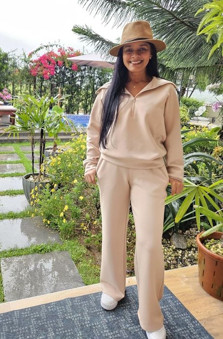 A reviewer enjoying the outdoors in a lush garden, dressed in a beige pantsuit and wide-brim hat, beaming at the camera.