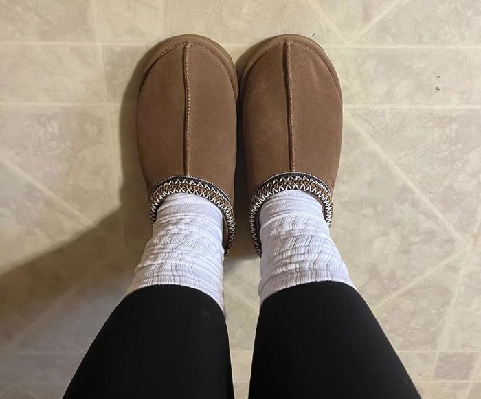 Feet in cozy brown slippers and white socks resting on a tiled floor.