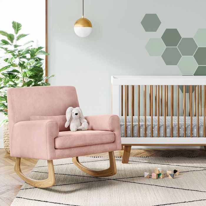 A pink rocking chair with a bunny stuffed animal placed in a nursery setting.