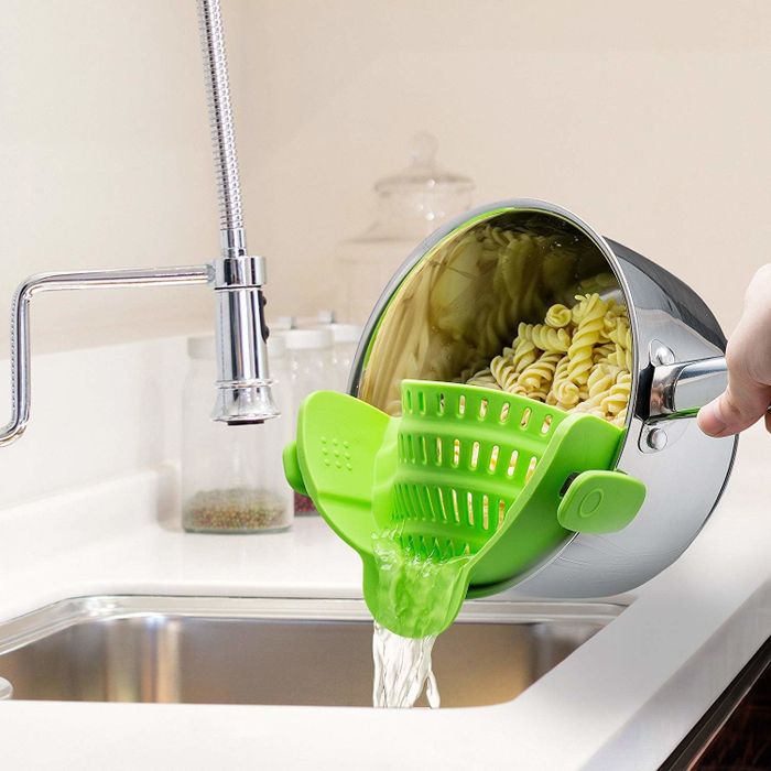 A green silicone strainer clipped to a pot containing rotini pasta