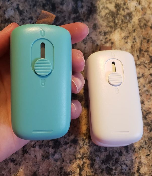 A reviewer showing off a compact blue sealer with a single button on it