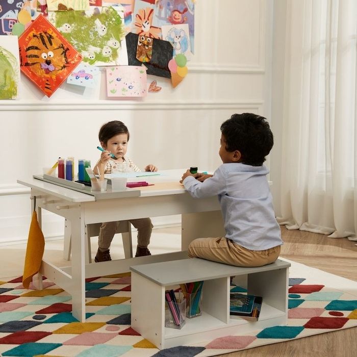 Two children seated across from each other, enjoying a coloring session at an art table placed atop a geometric rug.