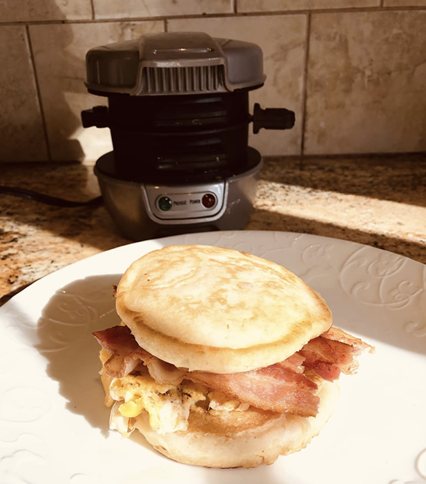 An egg, bacon, and cheese sandwich placed in front of a cylindrical metal cooker.