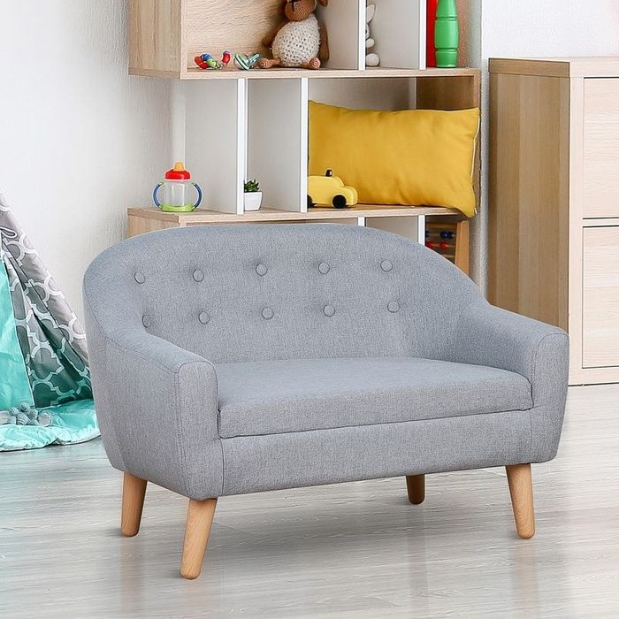 A small grey couch placed in front of a shelf filled with toys.