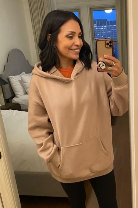 A reviewer takes a mirror selfie, sporting a beige hoodie and looking comfortable.