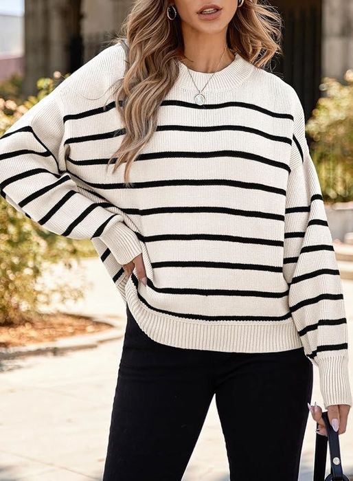 A model is outdoors, wearing a black and white striped sweater paired with black pants and carrying a handbag.