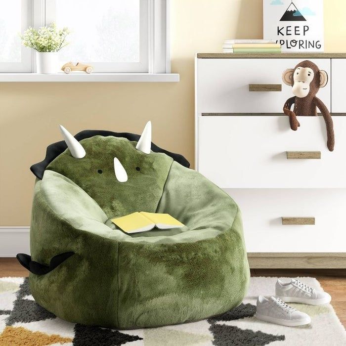 A dinosaur-themed bean bag chair sitting on a geometric rug next to a set of drawers