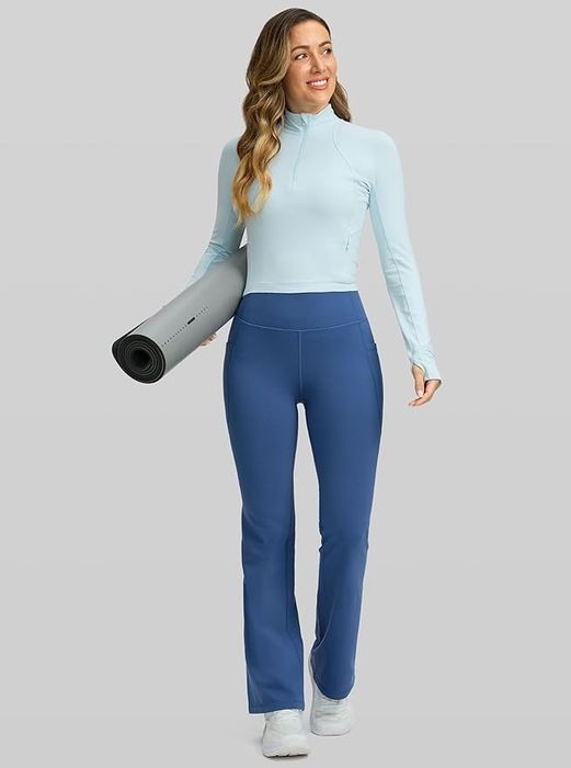 A person in athletic wear holds a yoga mat, wearing a form-fitting top and flared yoga pants.