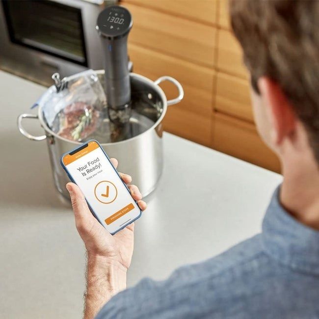 A model showcasing the sous vide cooker alongside the connected phone app, which helps manage cooking temperatures and times.