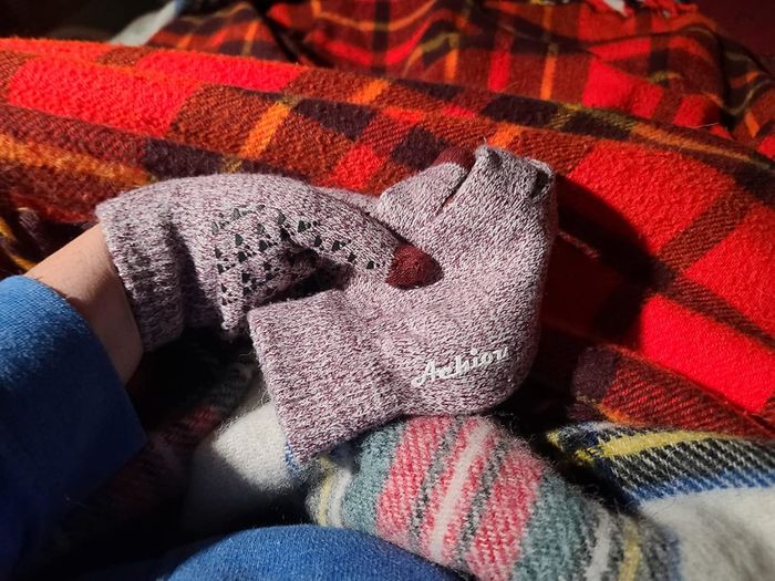 A cozy pair of knitted gloves placed on a plaid blanket. No identifiable text.