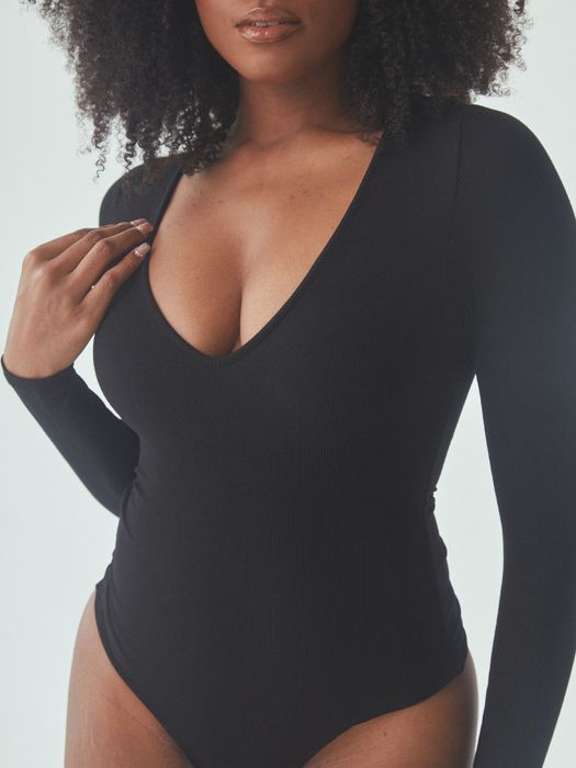 A woman confidently poses in a sleek black long-sleeve V-neck bodysuit for a shopping feature article.
