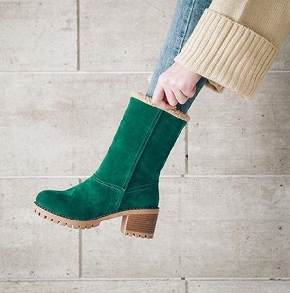 The green suede boot with a sleek turn-up design reaching the mid-calf level.