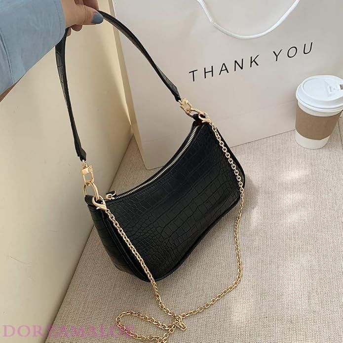 A chic small black handbag with a gold chain strap is displayed on a surface.