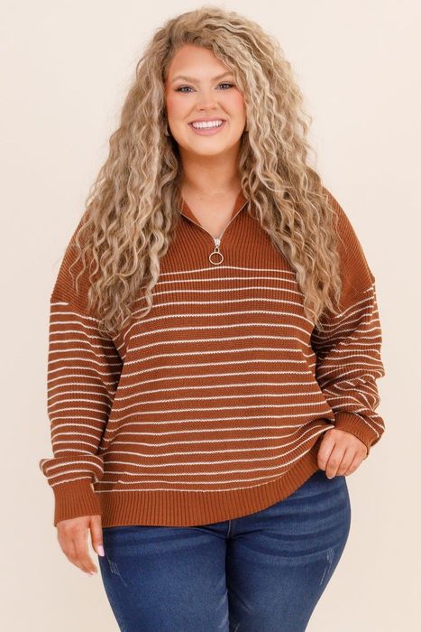 A model is smiling while wearing a cozy, striped pullover sweater and jeans.