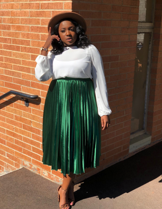 A reviewer wearing the dark green satin skirt paired with a white long-sleeve top and a hat.