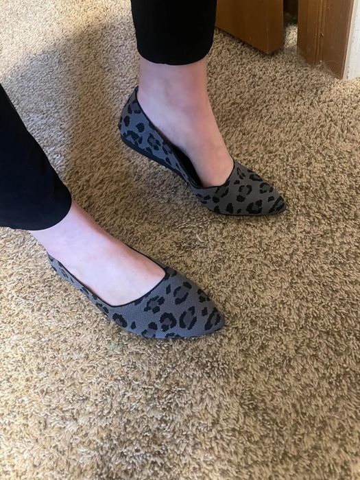 Person wearing gray leopard print flats with black leggings, standing on a carpet