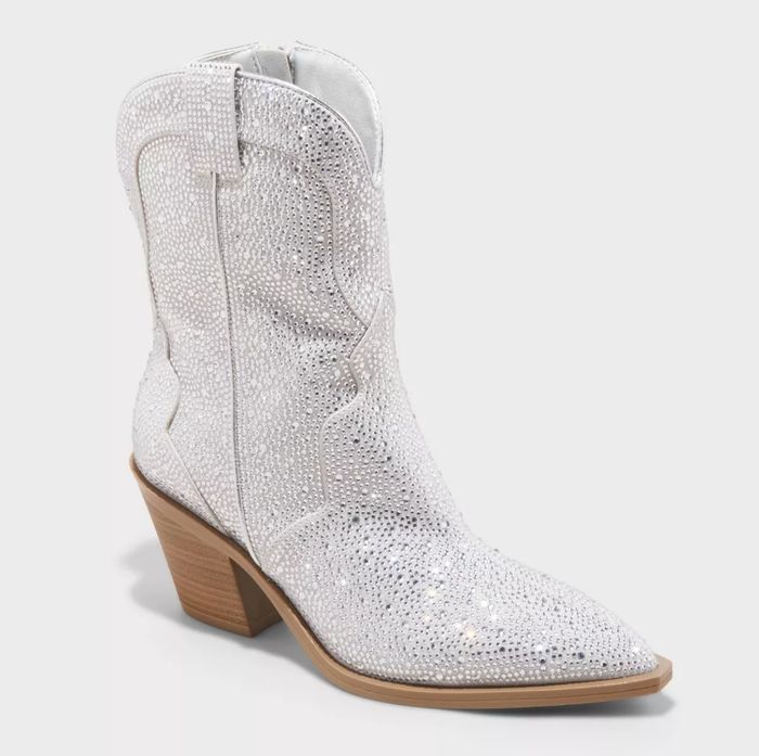 A white cowboy boot, featuring sparkling rhinestones and a wooden block heel.