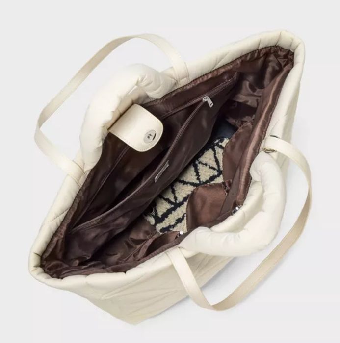 An open off-white quilted handbag showing its interior lining, a zipper pocket, and a patterned item placed inside.
