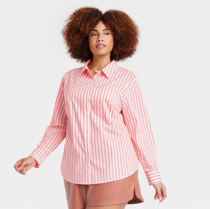A person with curly hair wearing a long-sleeve, striped button-down shirt paired with shorts