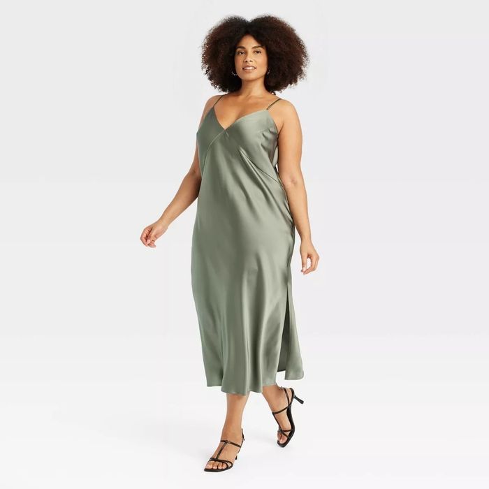A model styled in a sleeveless, V-neck satin slip dress featuring a slit, paired with delicate strappy sandals.