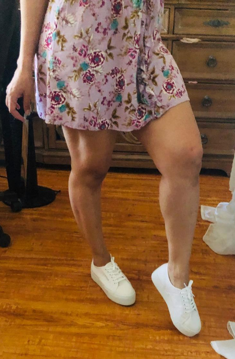 A reviewer takes a mirror selfie, sporting a floral dress and white sneakers. Only their legs and part of the dress are visible, with their face not shown.