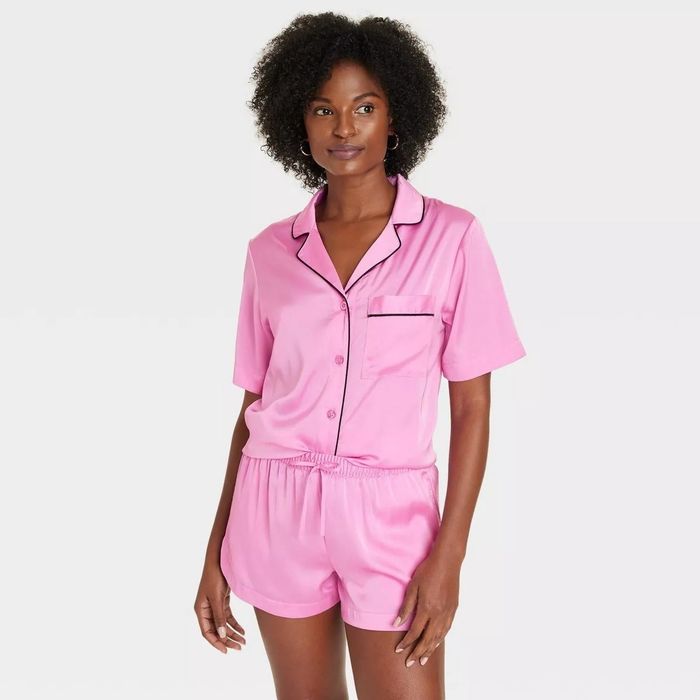 A person wearing a silky pink pajama set with short sleeves and shorts, posing against a plain backdrop
