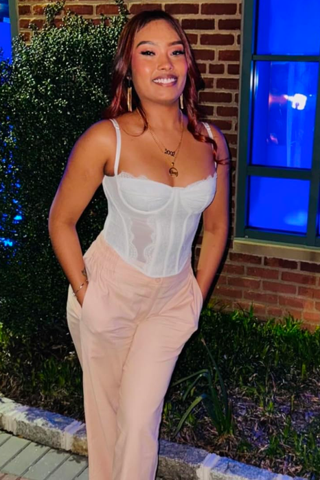 A reviewer stands outside a building at night, smiling with her hands in her pockets. She's wearing a white corset top and beige pants.