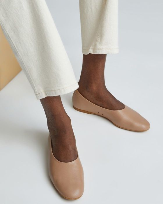a model dressed in off-white pants and light brown leather loafers with flat toes