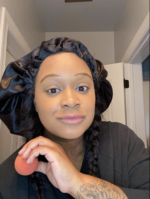 A reviewer blending foundation on their face with a makeup sponge