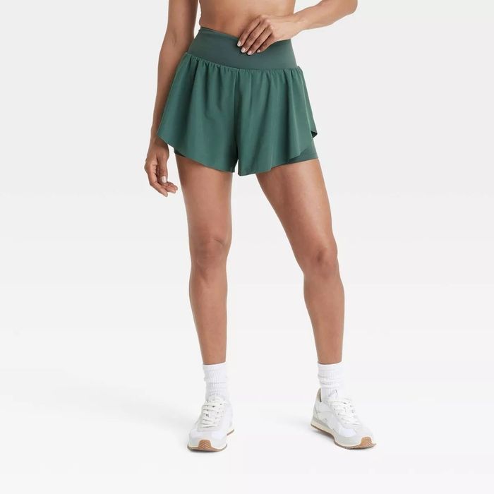 A model is sporting high-waisted athletic shorts with a breezy overlay paired with white sneakers. This look features in an article about the best shopping picks.