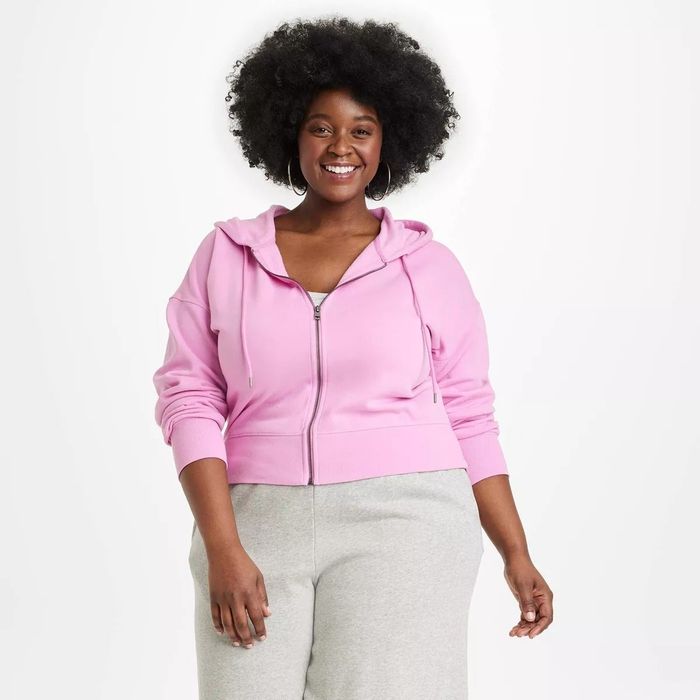 A person is smiling while wearing a zip-up hoodie and relaxed-fit pants, looking directly at the camera.