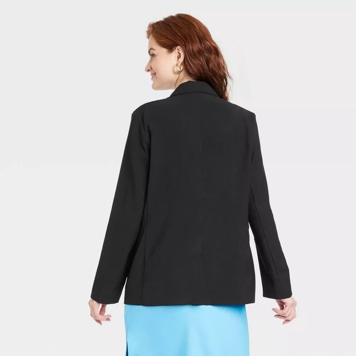 A person with red hair seen from behind, wearing a black blazer and a blue skirt
