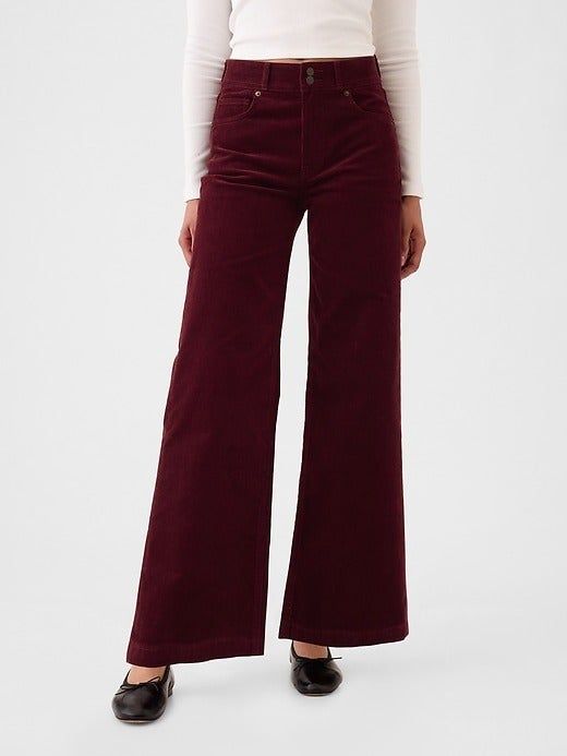 A model rocks high-waisted, flared corduroy pants paired with a white long-sleeve top and black shoes.